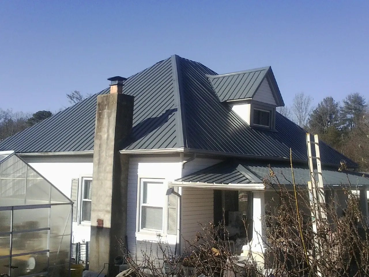 Dark blue standing seam metal roof on a white farmhouse with dormer — Slate & Tile Roof Repair by Roofing Brothers in Clive