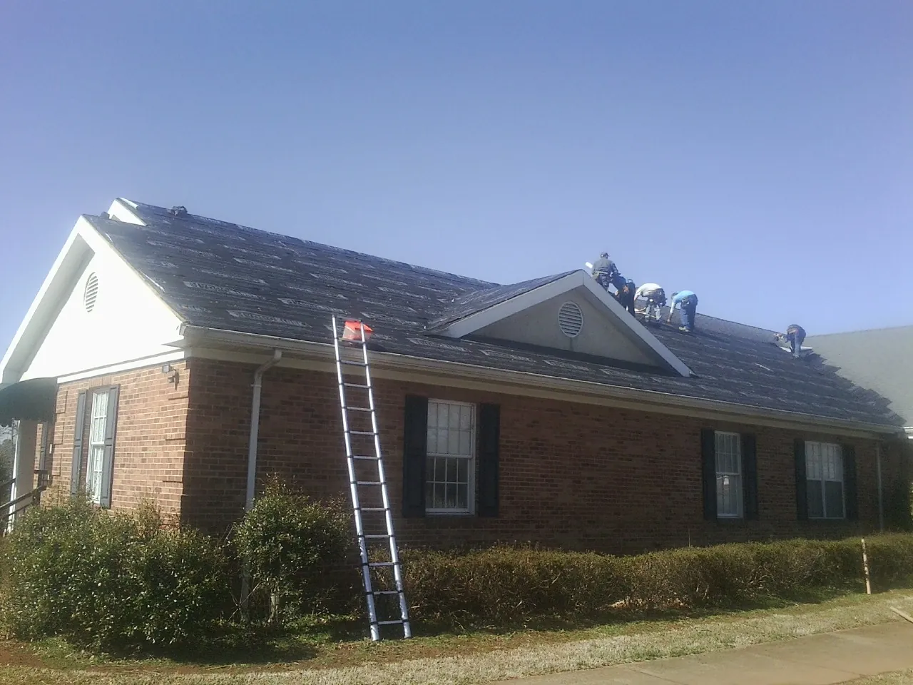 Crew tearing shingles off a brick ranch roof with a ladder set — Metal Roof Repair work by our crew in Clive