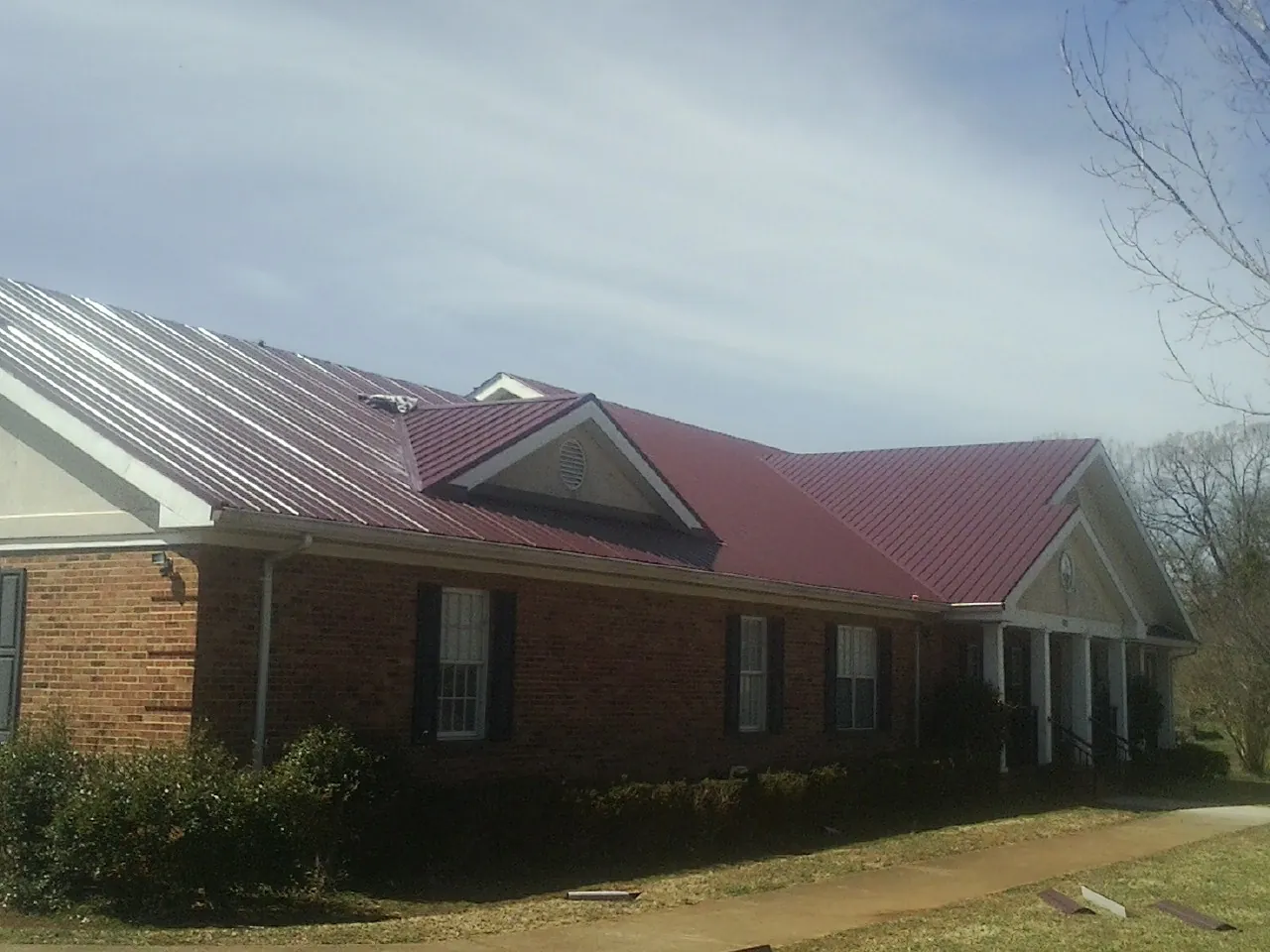 Red metal roof with gabled entries on a long brick building, from a Hail Damage Roof Repair job in Clive