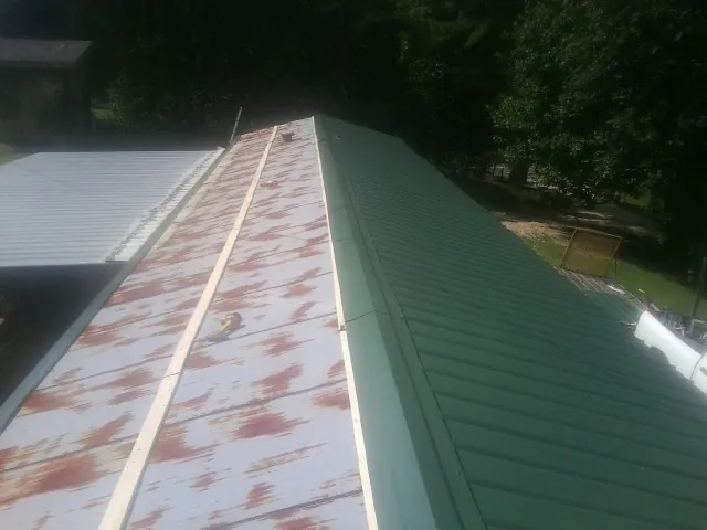Old rusted panels beside newly installed green metal roofing — Wind Damage Roof Repair by Roofing Brothers in Clive