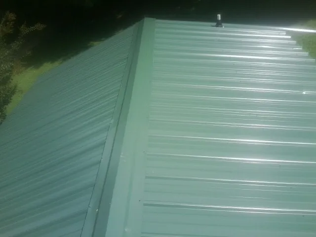 New green metal panels meeting at the ridge of a roof — Flat Roof Repair work by our crew in Clive