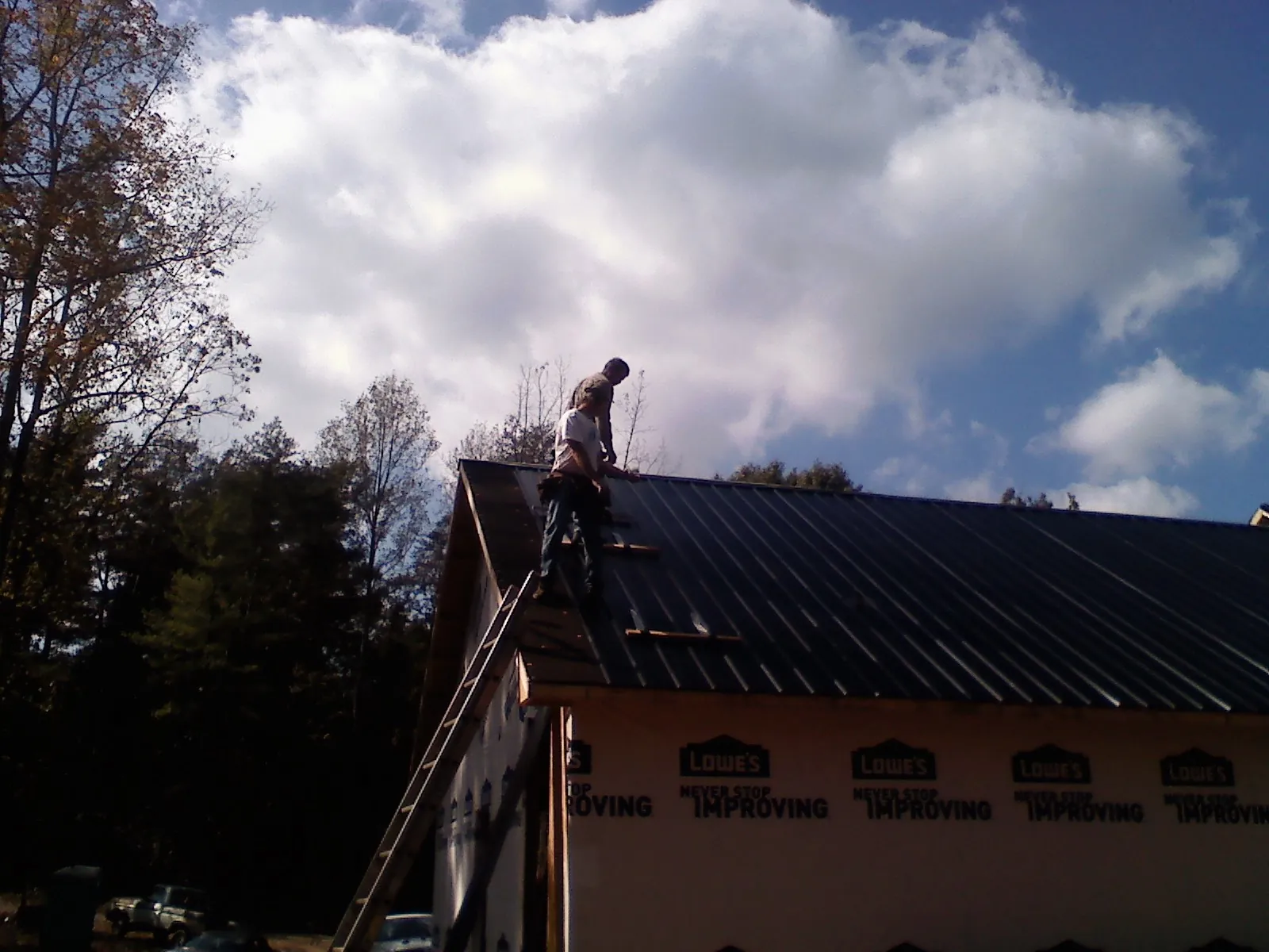 Roofer fastening dark metal panels high against a cloudy sky, from a Roof Inspection job in Clive