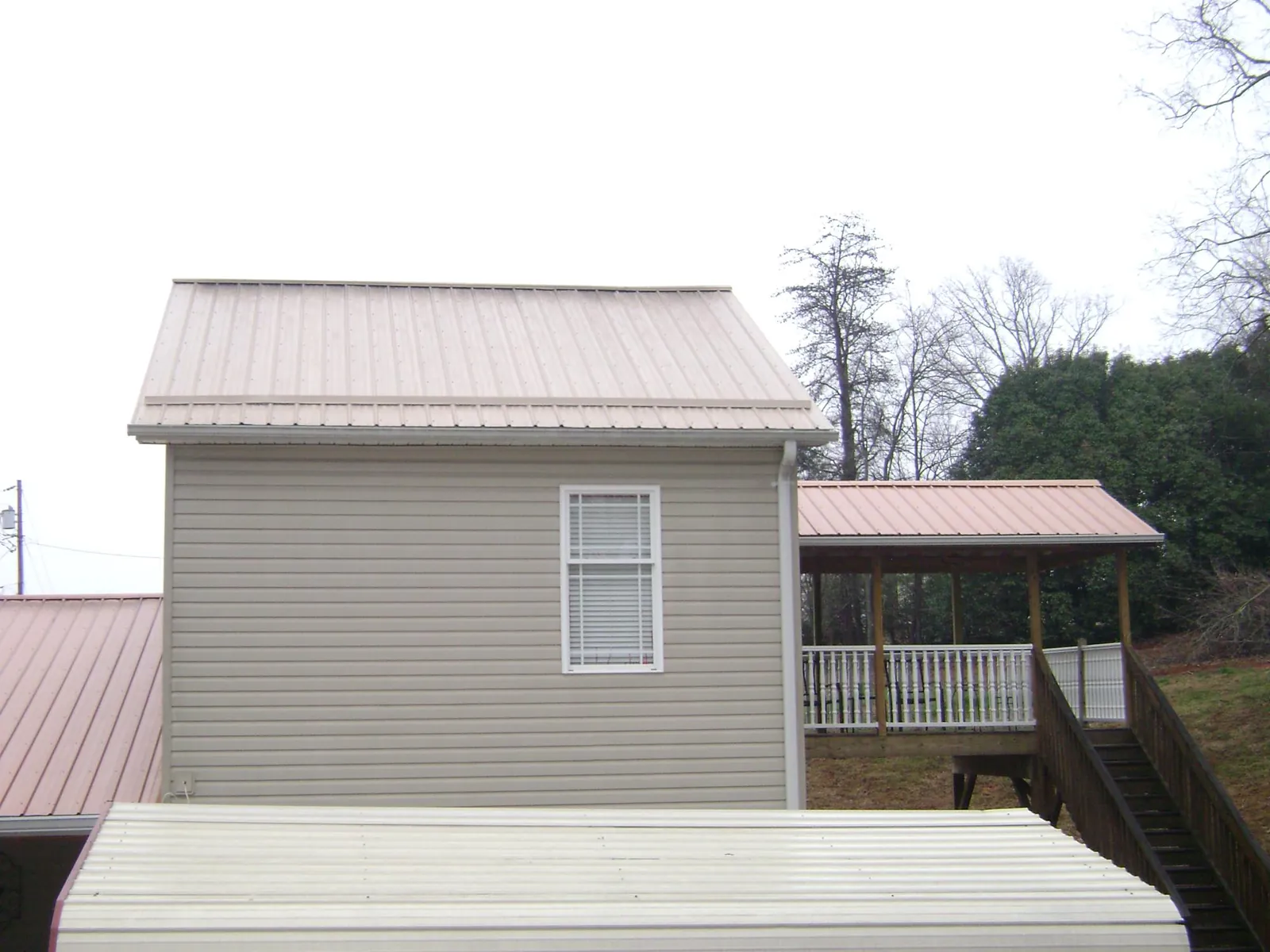Tan metal roofs on a two story addition and attached porch, from a Roof Replacement job in Clive